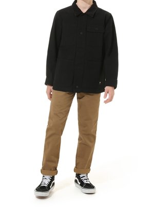 Chaqueta negra con cuello de pana, botones frontales y dos bolsillos grandes, combinada con pantalones beige y zapatillas negras con detalles blancos.