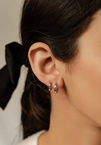 Srebrne kolczyki w kształcie kółek prezentowane na uchu, charakteryzujące się polerowanym wykończeniem oraz gładkim, zaokrąglonym kształtem. Minimalistyczny styl, lekkie wrażenie.