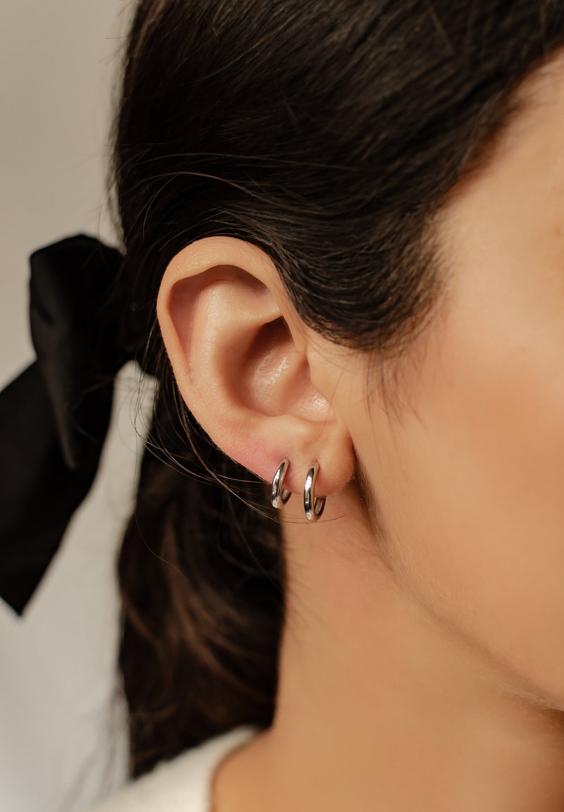 Srebrne kolczyki w kształcie kółek prezentowane na uchu, charakteryzujące się polerowanym wykończeniem oraz gładkim, zaokrąglonym kształtem. Minimalistyczny styl, lekkie wrażenie.