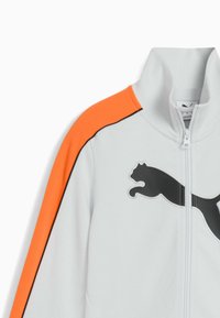 Witte jas met grijs Puma-logo, oranje schouderstreep en zwarte bies. Hooggesloten ontwerp met rits. Gladde textuur.