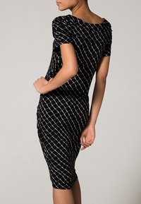 Svart figurnära klänning med korta ärmar och ett rutmönster i vitt. Har en rundad rygg och en strukturerad tyg.