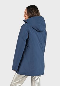 Marinblå huvjacka med zip-framsidan, rak passform och vattentätt material. Har sömdetaljer och en minimalistisk design.