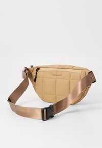 Quilted beige fabric bag with a rounded shape, a zippered front pocket, and a wide, adjustable beige strap.
