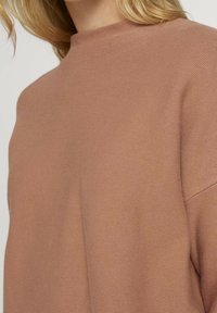 Strickpullover in warmem Mauve mit hohem Kragen, ausgestattet mit einer strukturierten Oberfläche und lockerem Schnitt im Brust- und Schulterbereich.