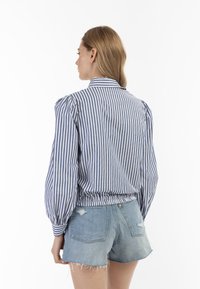 Stribet skjorte i blå og hvid bomuld med pufærmer og fitted talje, kombineret med lyse denimshorts med revnede kanter.