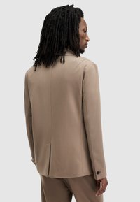 Blazer estructurado beige con una sola abertura en la espalda, solapas de pico y puños abotonados. Tela suave con un corte entallado.