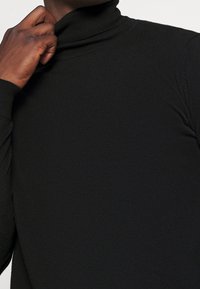 Pull à col roulé noir avec une coupe ajustée. Tissu en maille douce, texture lisse, avec un col haut et des manches longues. Style simple et minimaliste.