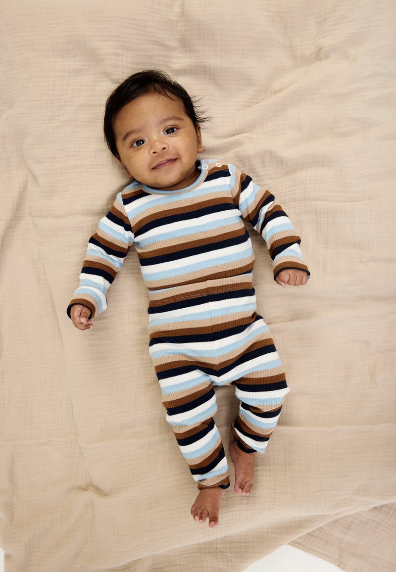 Dryžuotas ribb ventilis su šviesiai mėlynos, rudos ir tamsiai mėlynos spalvų juostelėmis, ilgomis rankovėmis ir spaustukais prie apykaklės, dėvimas besišypsančio kūdikio.