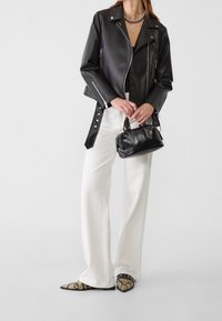 Sort motorcykeljakke i imiteret læder med sølvlynlåse, kombineret med hvide bukser med vide ben og mønstrede flade sko med spidse tæer. Sort håndtaske med nitter.