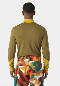 Olijfgroene langemouwen shirt met gele kraag en accenten. Gestructureerde stof met een getailleerd ontwerp, gedragen met gemusterde meerkleurige broeken.