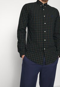 Knappskjorta i mörkgrönt med ett rutigt mönster i rött och gult. Tillverkad i bomull med klassisk krage och långa ärmar.