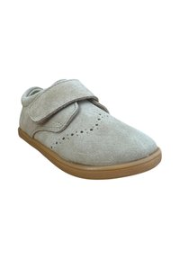 Zapato de ante gris claro con punta redondeada, dos tiras de velcro, perforaciones decorativas y suela de goma beige.