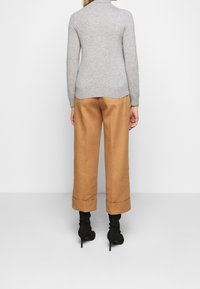 Gray, long-sleeve sweater with a high collar paired with brown, wide-leg trousers rolled at the cuffs, worn with black heeled boots.