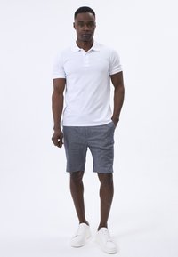 Bílá polo tričko s límečkem, zkombinované s šedými šortkami s jemnou texturou a bílými teniskami. Jednoduchý, neformální outfit.