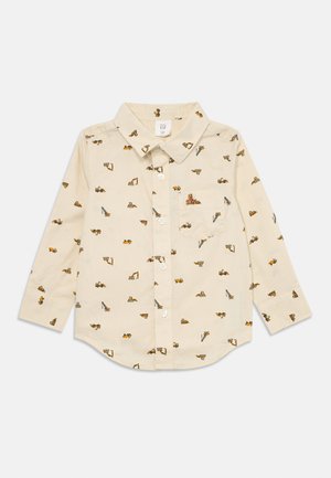 Camisa beige de manga larga con cuello abotonado, que presenta un estampado repetido de vehículos de construcción en varios colores. Incluye un bolsillo en la parte frontal.