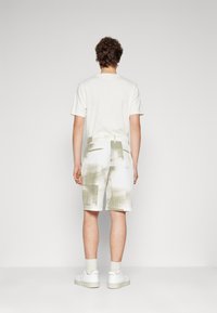 White, textured shorts with a green grid pattern, elastic waistband, and pockets. Worn with a light-colored, short-sleeved shirt and sneakers.