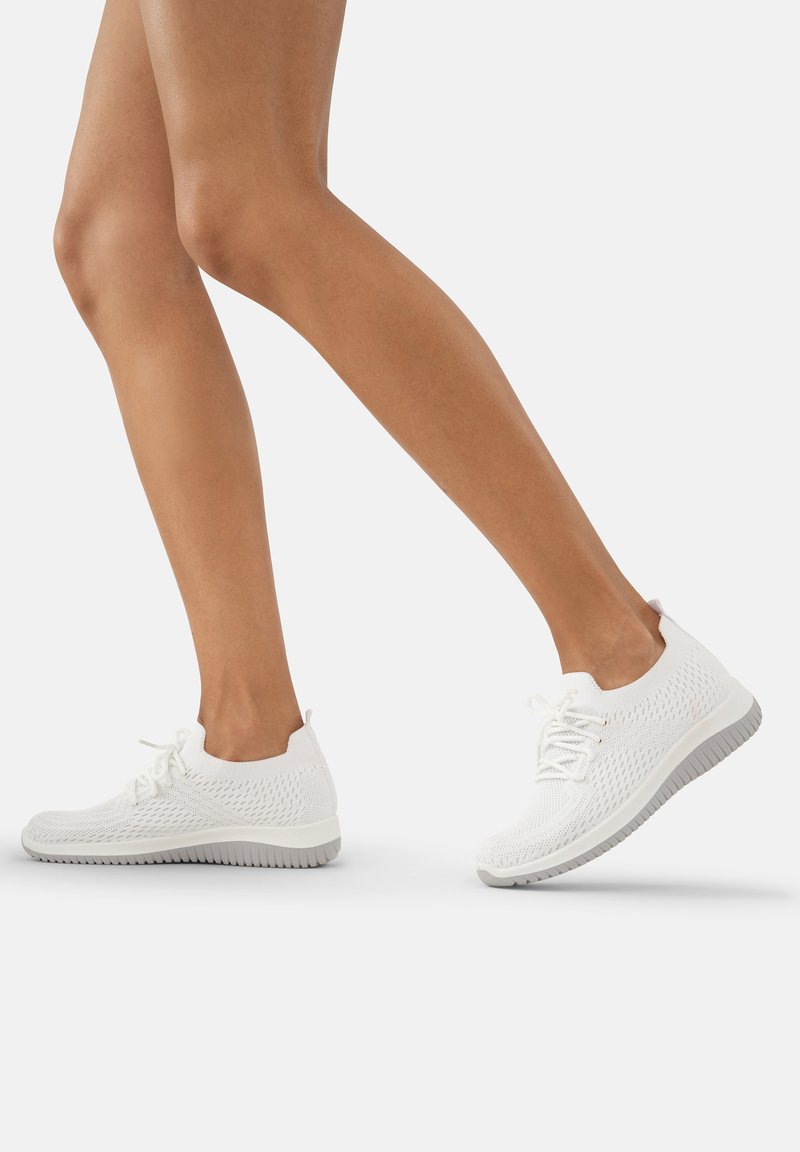 Baskets de sport en tricot blanc avec un dessus texturé, un col rembourré et une semelle en caoutchouc flexible, présentant un design à lacets et un branding minimal.