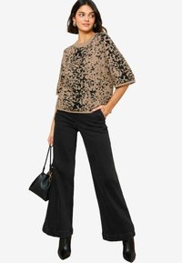 Top de punto corto de manga corta en color beige y negro con un patrón, combinado con jeans de pierna ancha negros y botas de tacón negras, sosteniendo un bolso negro.
