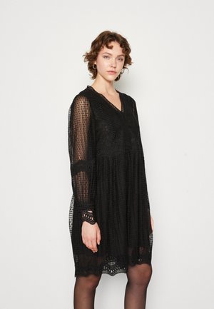 Black dress made of textured lace with long sleeves, a V-neck, and intricate embroidery along the bodice and hem. Loose fit.