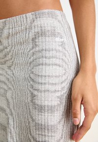 Grått tyg i närbild med ett texturerat mönster med horisontella linjer. En vit "obey"-logotyp syns på högra sidan.