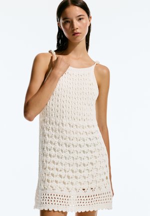 Robe au crochet en crème avec un motif texturé, sans manches, et des bretelles réglables. Comprend un ourlet festonné et une trame ouverte.