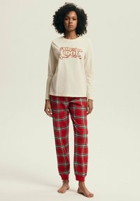 Kremowa koszula z długim rękawem z grafiką "stay cool", w połączeniu z czerwonymi spodniami piżamowymi w kratę, z zielonymi i białymi akcentami oraz ściągaczami.