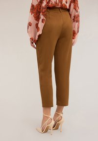 Pantalon marron ajusté avec une finition lisse, taille cintrée et jambes effilées, associé à des chaussures à talons nude avec des brides de cheville.
