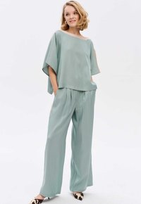 Lichtgroene blouse met brede mouwen, gecombineerd met bijpassende losse broek. Glad textuur met een relaxte pasvorm, met zijsplitten.