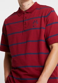 Polo rayé rouge et marine, en coton, manches courtes, patte de boutonnage à trois boutons, logo brodé sur la poitrine gauche.