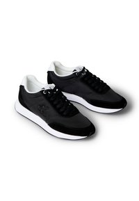 Schwarz-weiße Low-Top-Sneaker mit schwarzen Schnürsenkeln und "CK"-Logo an der Seite, ausgestattet mit gepolsterten weißen Sohlen und gepolsterten inneren Kragen.