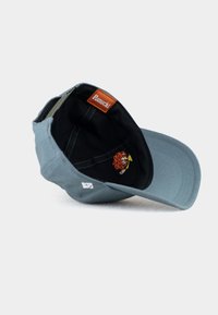 Blue fabric cap with a curved visor. Interior features a black lining and orange brand tag. Embroidered design of a colorful character on the inside.
