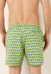 Pantaloni da bagno con vita elasticizzata, caratterizzati da uno sfondo giallo e un motivo di cactus ripetuto in verde e blu.