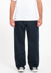 Dark blue denim pants with a loose fit, straight legs, and subtle texture. Worn with a plain white t-shirt and black sneakers.