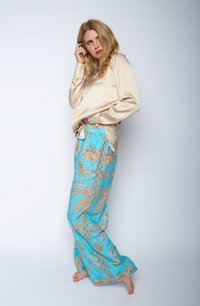 Seidenbluse in hellbeige, kombiniert mit weit geschnittenen Hosen mit blauem Hintergrund und beigen Blumen- und Blättermustern. Niedrig-kontrastierende Knöpfe sichtbar.