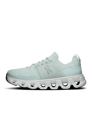 Hellgrauer Sportschuh mit gestricktem Obermaterial, Schnürverschluss und dicker weißer Sohle mit hohlen geometrischen Ausschnitten und schwarzen Außensohlenkanten.