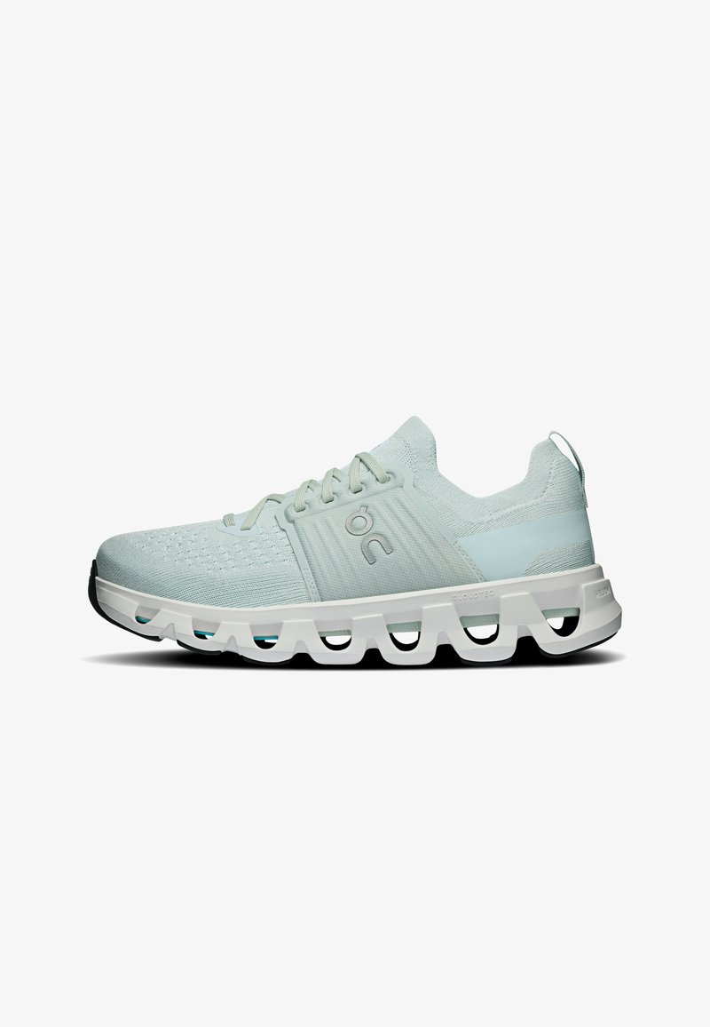 Chaussure de sport gris clair avec tige en maille, fermeture à lacets et semelle blanche épaisse comportant des découpes géométriques creuses et des bords noirs sur la semelle extérieure.