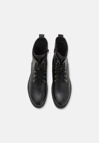 Par de botas de tobillo de cuero negro con cordones, con cremalleras laterales y tiradores, mostradas desde una vista superior sobre un fondo blanco.