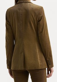 Hnědý kordový blazer s přiléhavým střihem, s klopami a knoflíkovými manžetami. Obsahuje zadní rozparek pro snadný pohyb a vroubkovanou texturu.