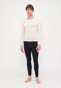 Dlouhý rukáv, přiléhavá off-white košile s kulatým výstřihem a malým předním knoflíkem; spárováno s černými, přiléhavými legínami.