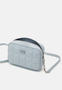 Světle modrá prošívaná crossbody taška se stříbrným logem, zipovým uzávěrem a odnímatelným řetízkem. Obdélníkový tvar; hladká textura.