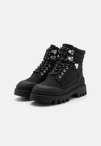 Botas negras hasta el tobillo con parte superior texturizada, suela de goma gruesa y herrajes plateados en contraste. Incluye cordones y un collarín acolchado.
