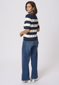 Haut en tricot rayé bleu marine et blanc à manches courtes, associé à un jean en denim bleu à jambes larges et des chaussures blanches à talons bloc.