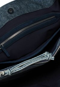 Pochette en denim avec un intérieur sombre, dotée d'une poche zippée en tissu bleu marine et d'un cordon tressé en accent, fermée par un bouton-pression.