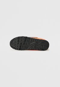 Nike-tennisovet med sort gummiyttersåle, som har rektangulære mønstre og en overdel som hovedsakelig er oransje med hvite detaljer.