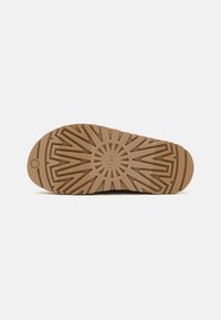 Semelle de chaussure en caoutchouc marron avec un motif en rayons de soleil, comportant des rainures pour l'adhérence et un bout arrondi. Logo gravé au centre.