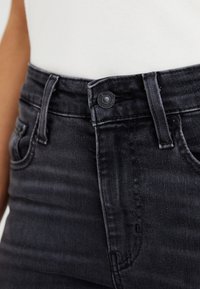 Black high-waisted jeans with a smooth texture, featuring a button closure and standard pockets. The fabric has a slight sheen.