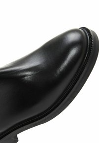 Stivaletto in pelle nera con texture liscia, punta arrotondata e dettagli di cucitura discreti lungo la suola. Design a tacco basso.