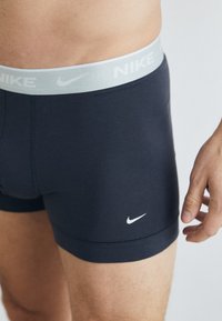 Fekete Nike boxer alsónadrág, világosszürke rugalmas derékkal, amelyen a logó látható. Az anyag sima, testhezálló, fehér logóval kiemelve.