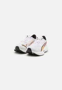 Zapatillas deportivas blancas con parte superior de punto texturizado, acentos en naranja y negro, y suela de goma. Presenta un cierre de cordones y un diseño de puntera redondeada.