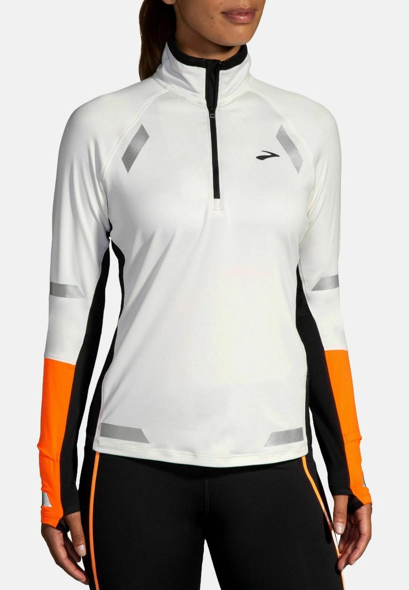 Maglietta atletica a maniche lunghe da donna, bianca con dettagli neri e arancioni, design a zip quarti, dettagli riflettenti, materiale sintetico elasticizzato.